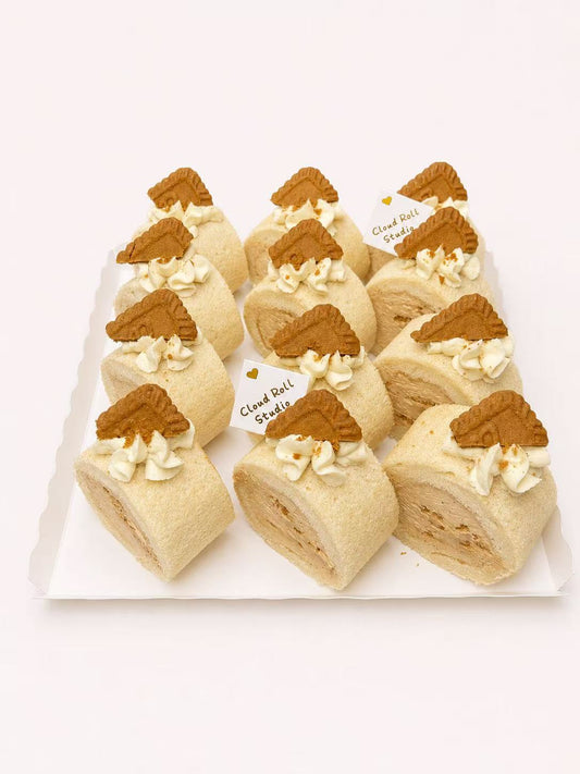 A set of ten cream-filled pastry rolls decorated with brown cookie pieces on top, arranged on a white rectangular plate against a plain white background.